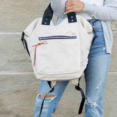 Person holding a beige backpack with a stone wall background