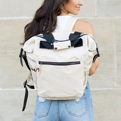 Woman wearing a beige backpack with black bows against a light stone wall.