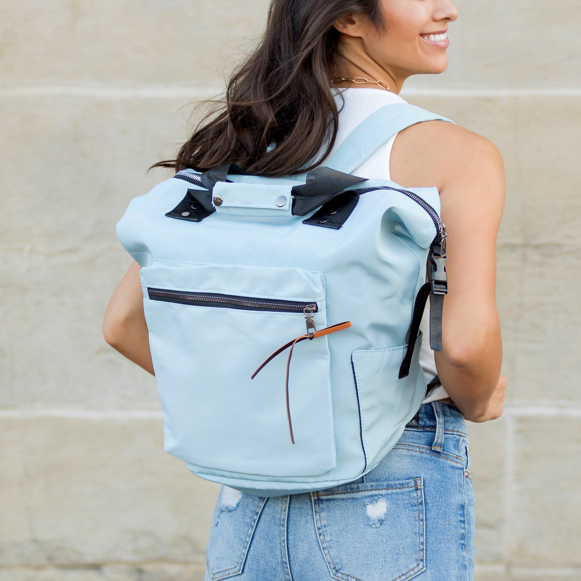 Woman wearing a light blue backpack with zippers against a beige wall.