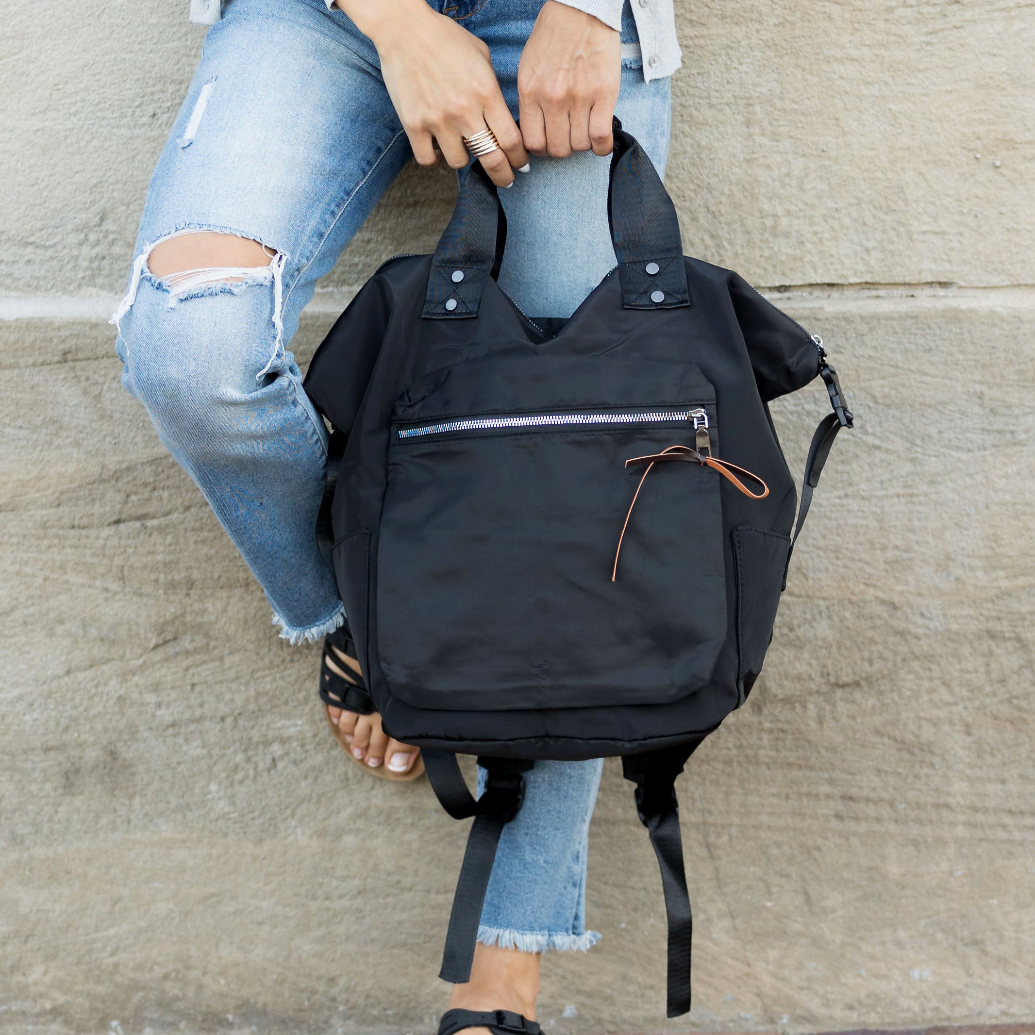 Person holding a black backpack against a concrete wall.