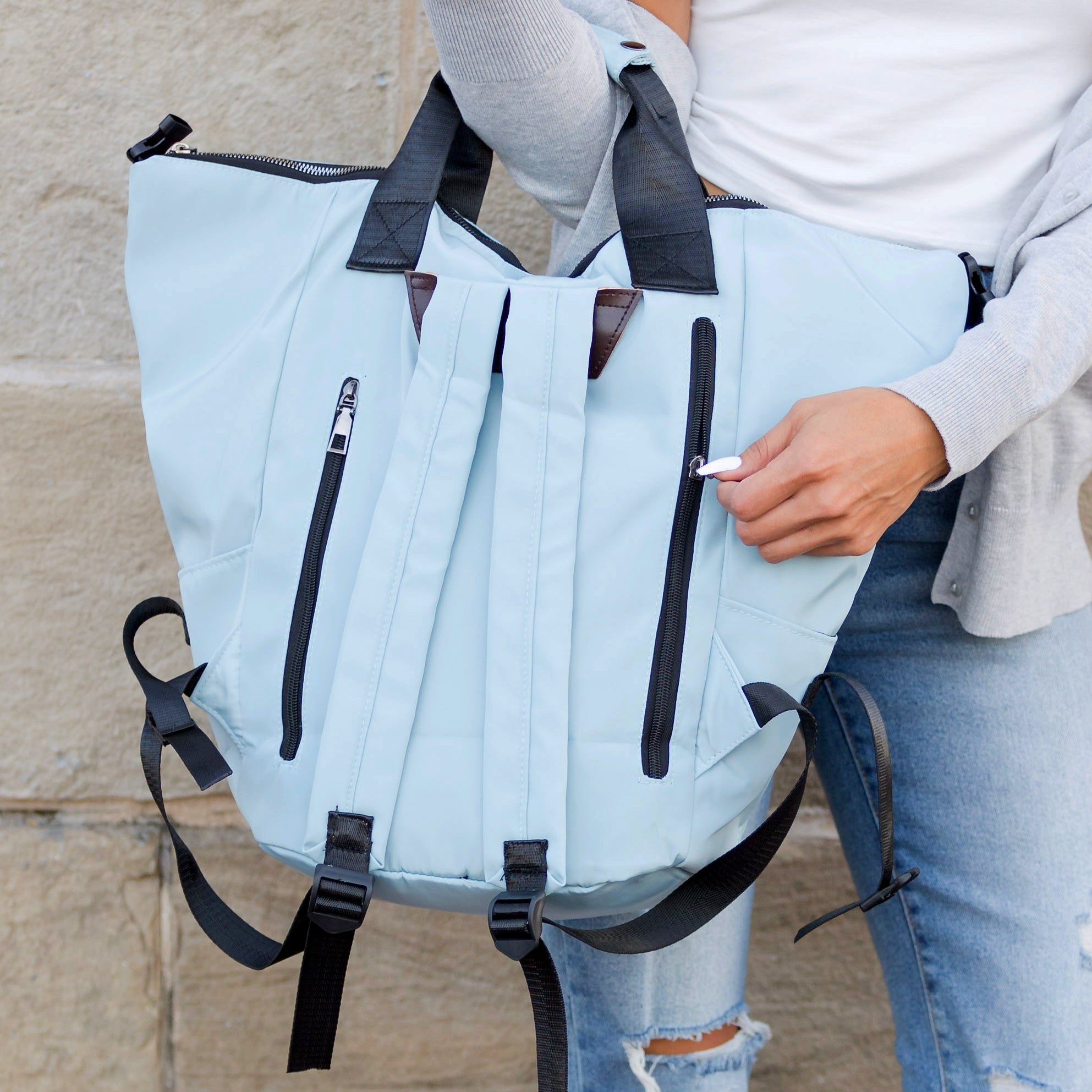 Light blue backpack with black zippers held by a person wearing a light gray sweater and jeans.