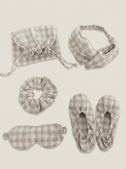 Set of gray plaid sleep accessories including a bonnet, headband, eye mask, slippers, and a drawstring bag on a beige background.