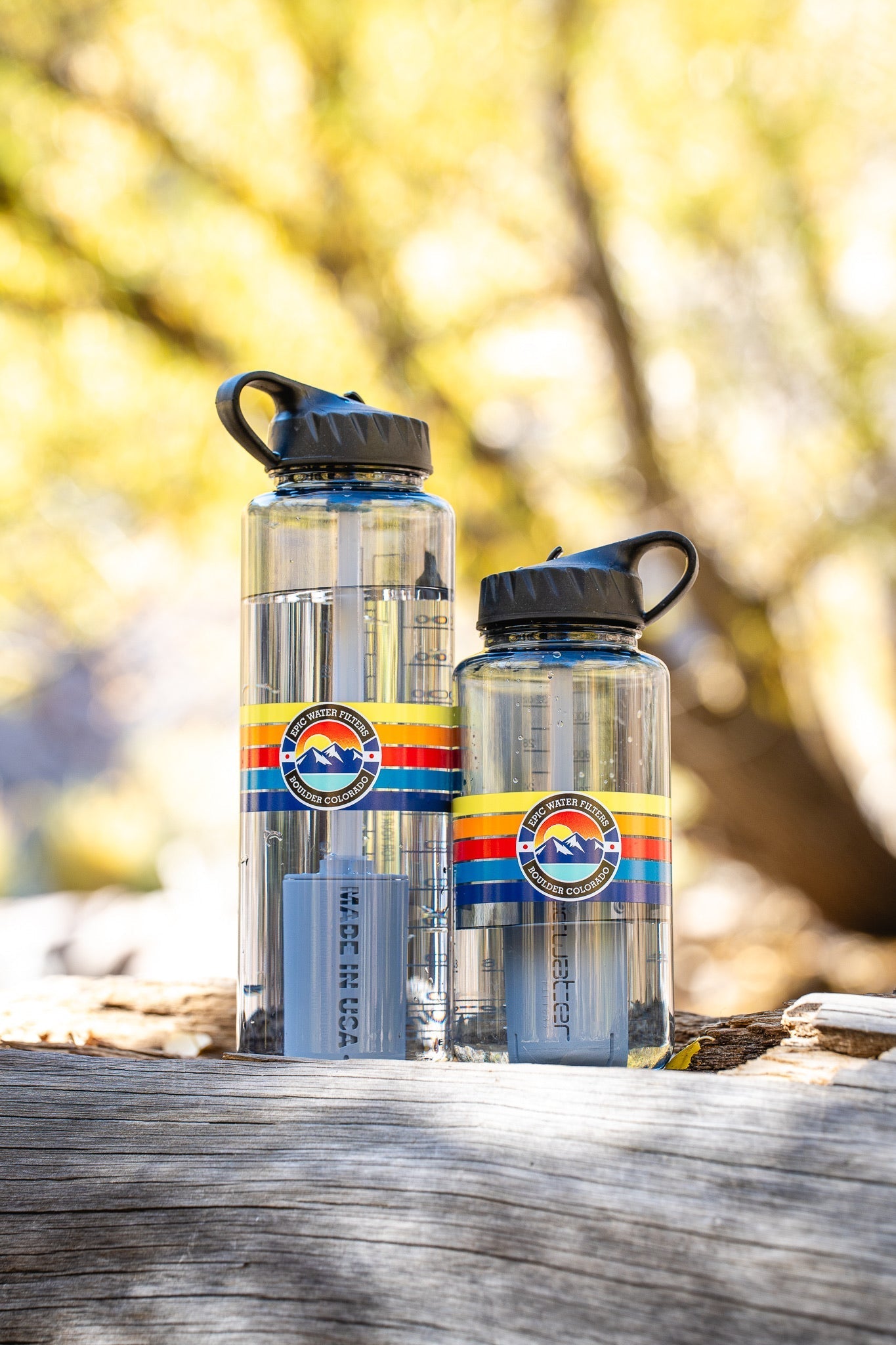 Two water bottles with colorful labels on a wooden surface with a blurred natural background