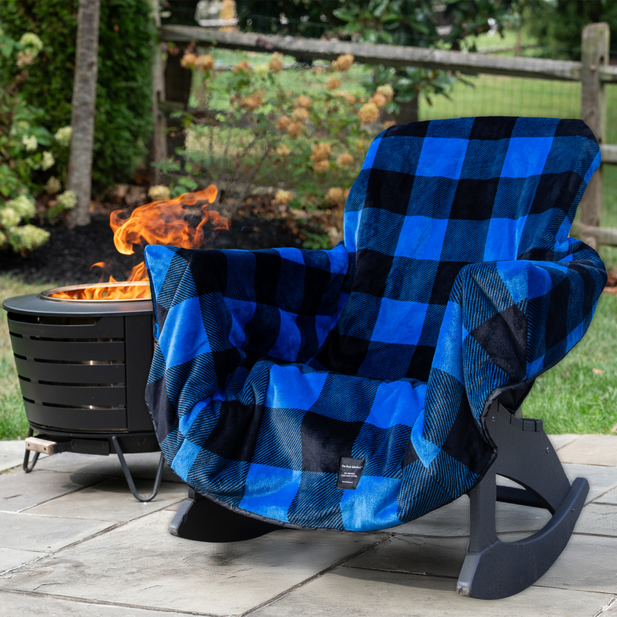 Blue and black checkered blanket draped over a chair by a fire pit in a garden setting
