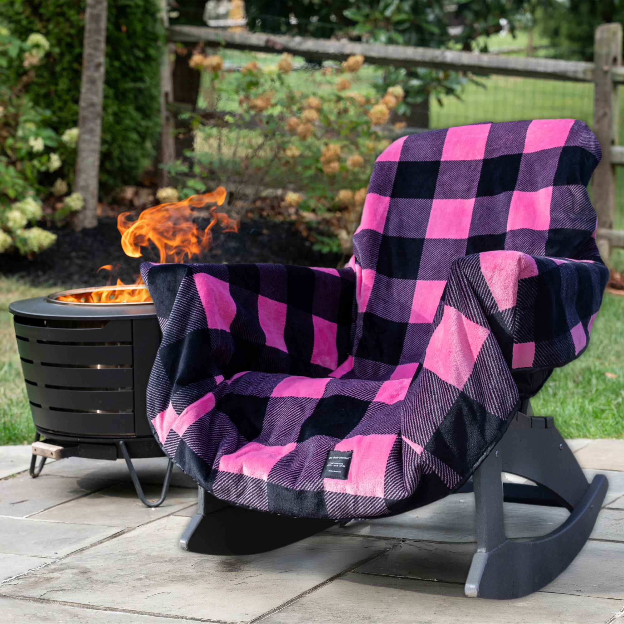 Black and pink checkered blanket draped over a chair by a fire pit in a garden.