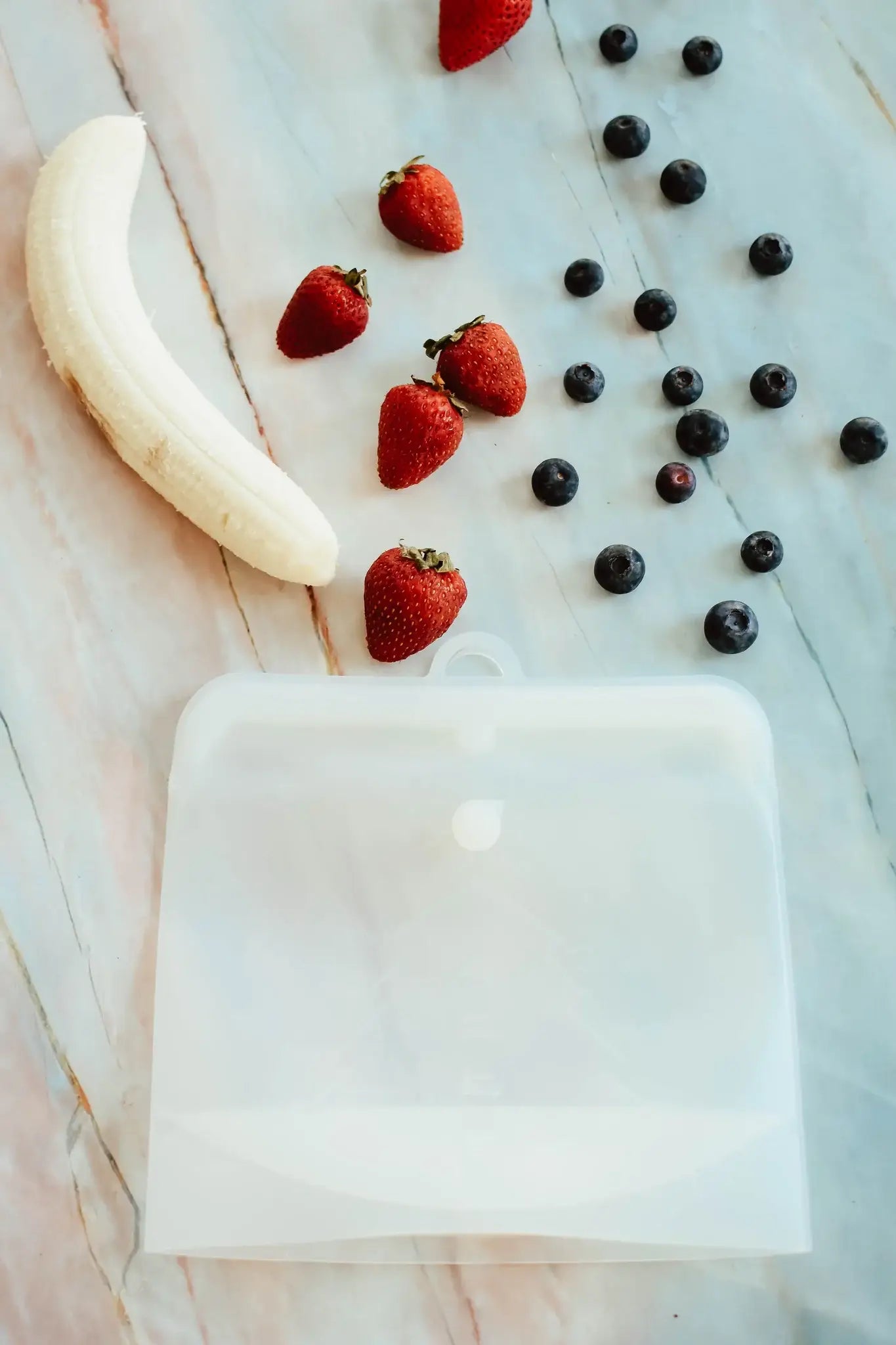 Fruit including strawberries, a banana, and blueberries on a marble surface.