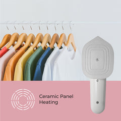 Handheld garment steamer with ceramic panel heating feature on a pink background, next to a rack of colorful clothes.