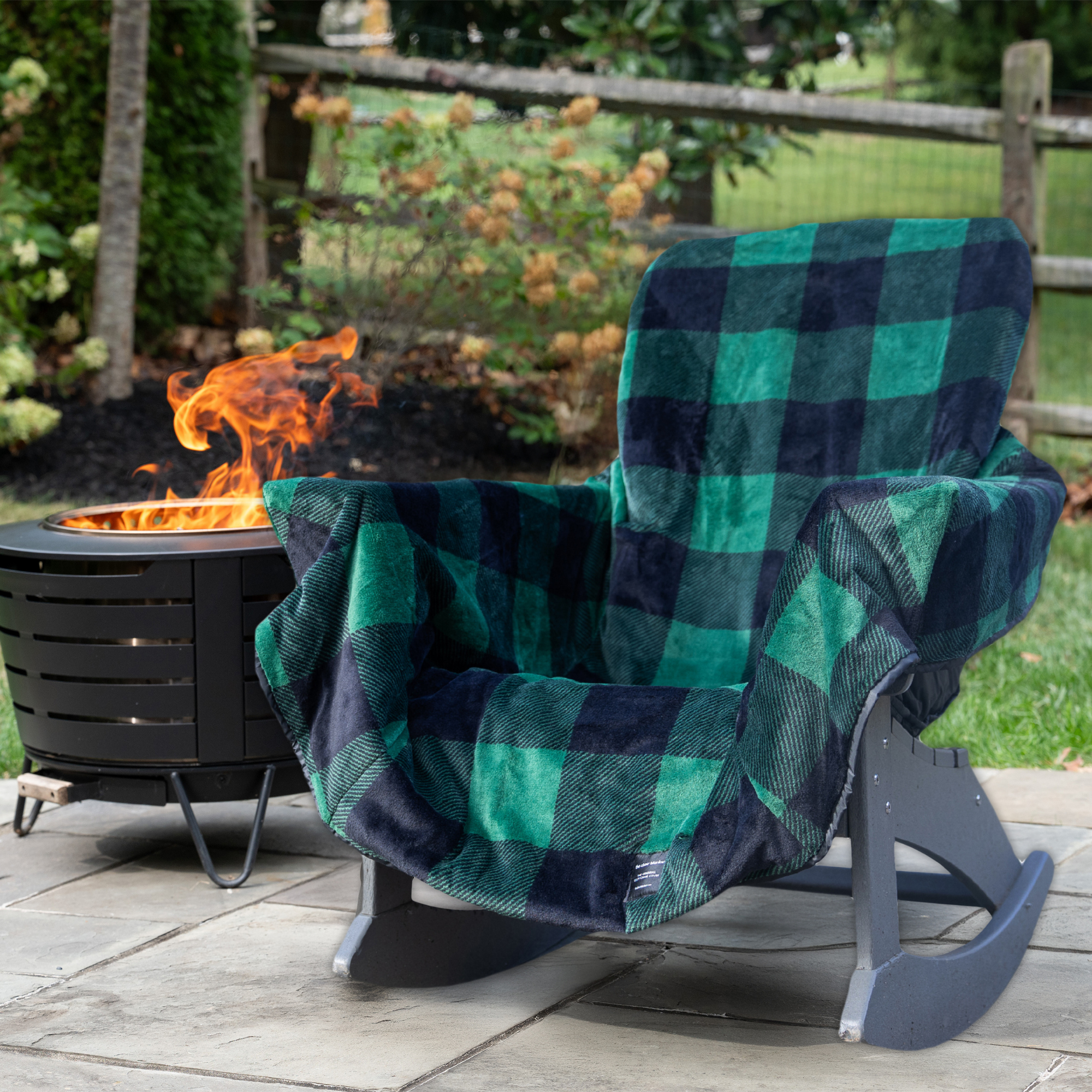 Green and blue checkered blanket draped over a chair next to a fire pit in a garden setting.