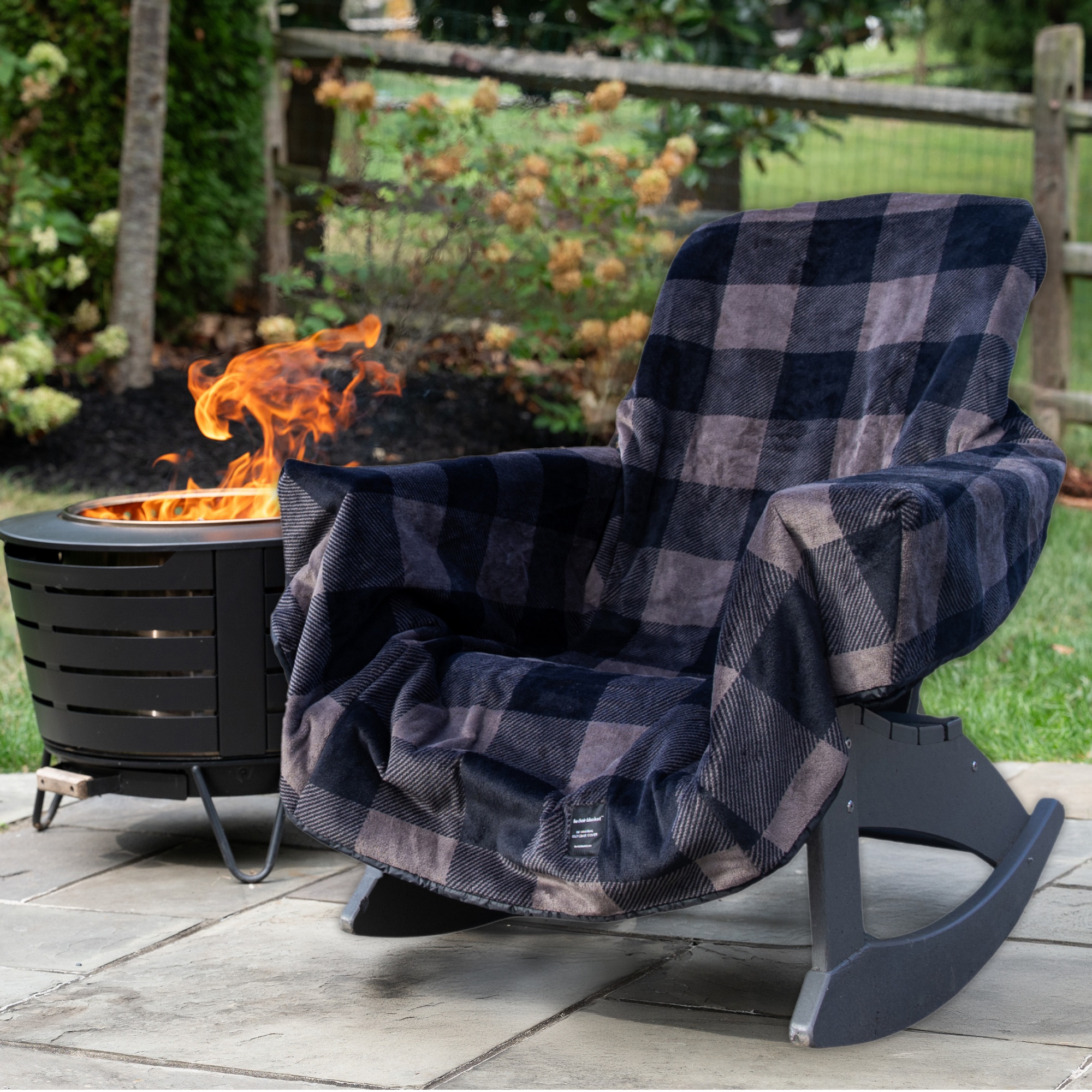 Black and gray checkered blanket draped over a rocking chair next to a fire pit in a garden setting.