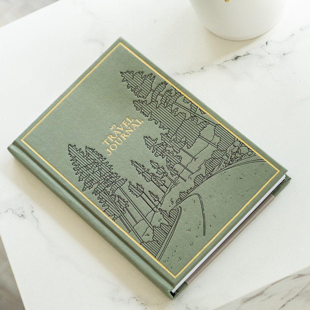 Green travel journal with embossed design on a marble surface