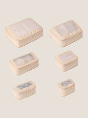 Set of six beige travel packing cubes with clear windows on a light beige background