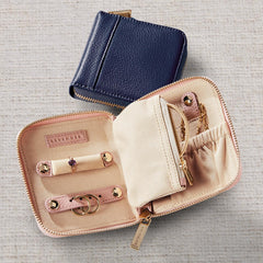 Open beige jewelry case with blue zipper pouch on a textured gray surface