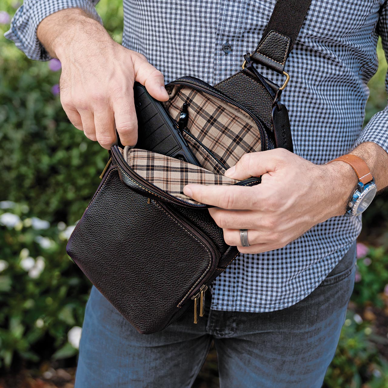 Person opening a black leather bag with plaid lining, wearing a checkered shirt and jeans.