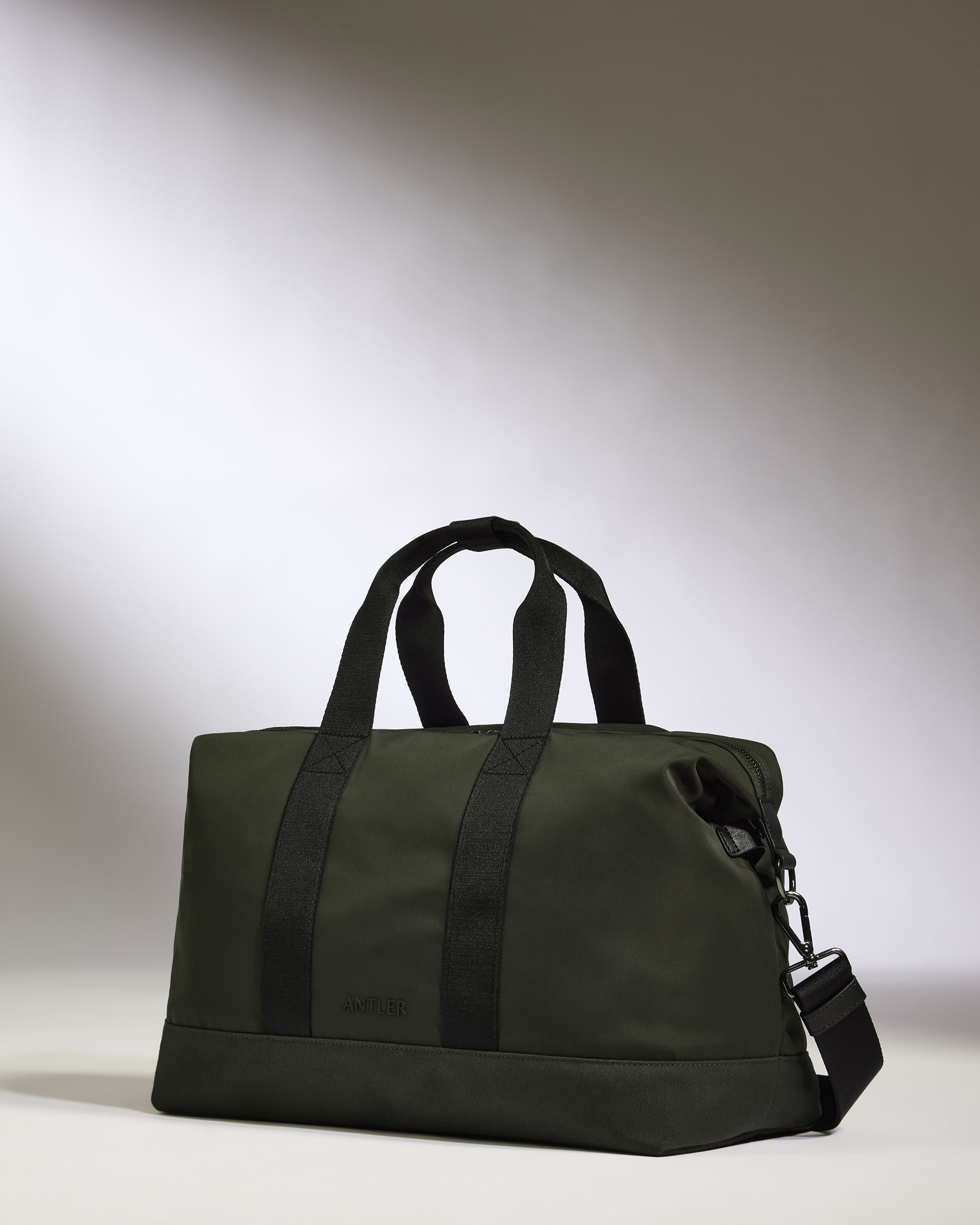 Green duffel bag with black handles and strap on a light gray background