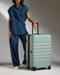 Person in blue outfit with a light gray suitcase on a plain background