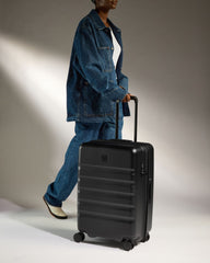 Person in blue denim outfit pulling a black suitcase against a neutral background