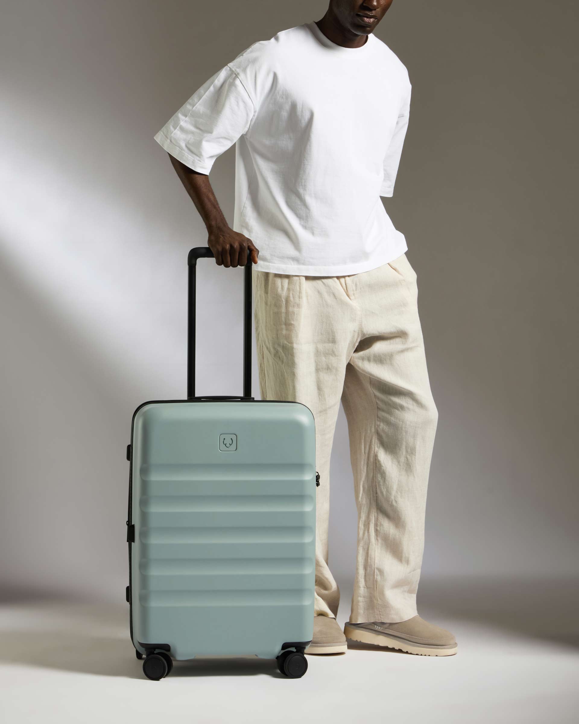 Person holding a light green suitcase against a neutral background