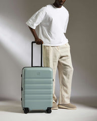 Person holding a light green suitcase against a neutral background