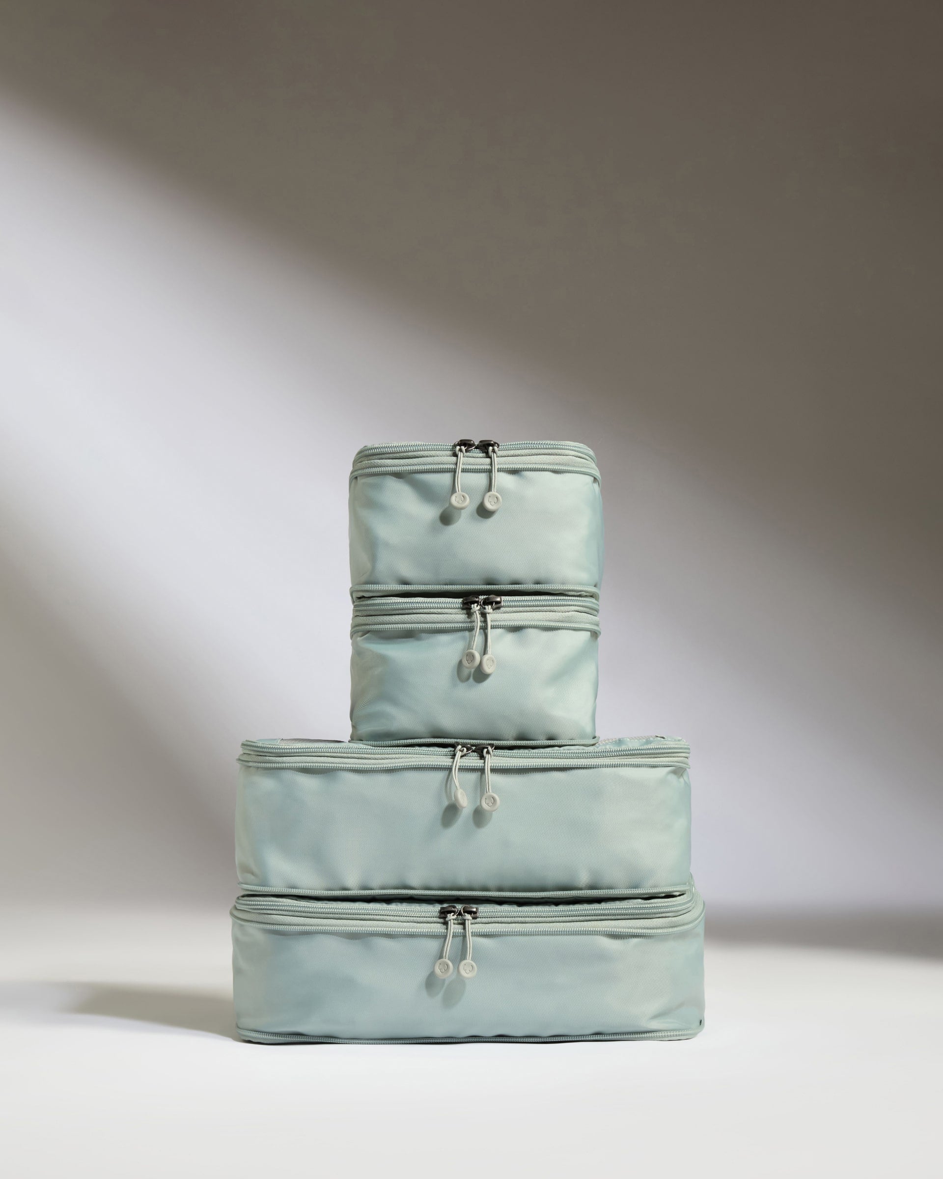 Set of three light blue travel bags stacked on a neutral background