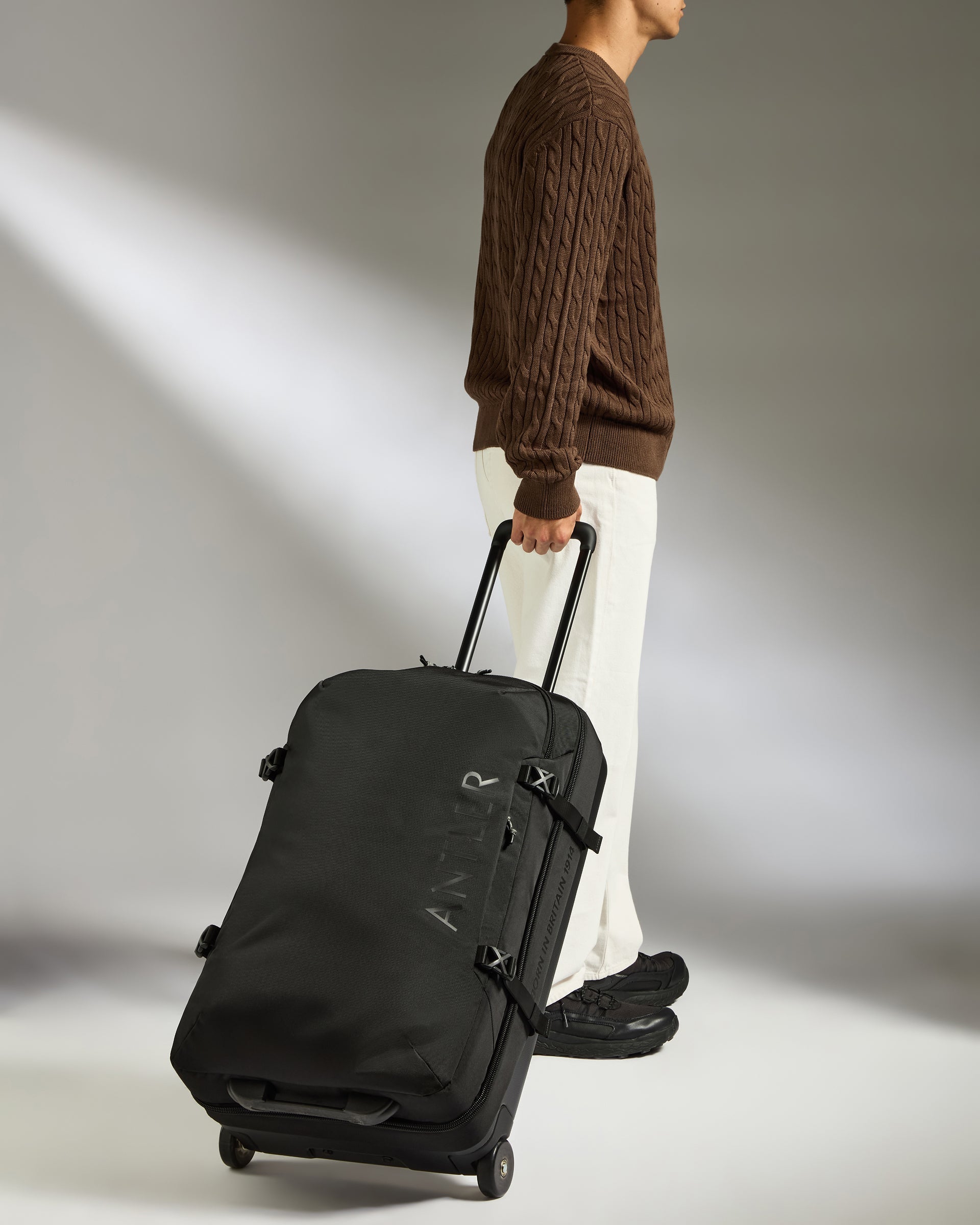 Person pulling a black suitcase on a plain background