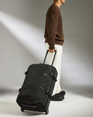 Person pulling a black suitcase on a plain background