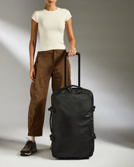 Person holding a black suitcase against a neutral background