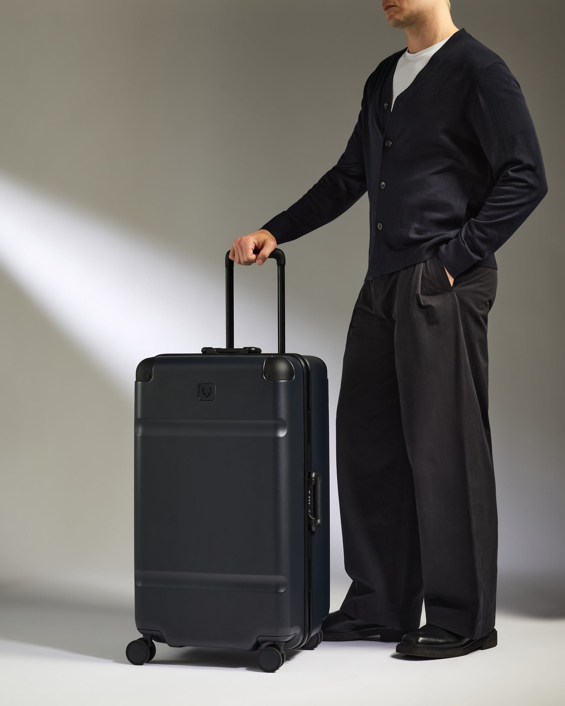 Man holding a black suitcase against a neutral background