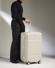 Person holding a beige suitcase against a neutral background