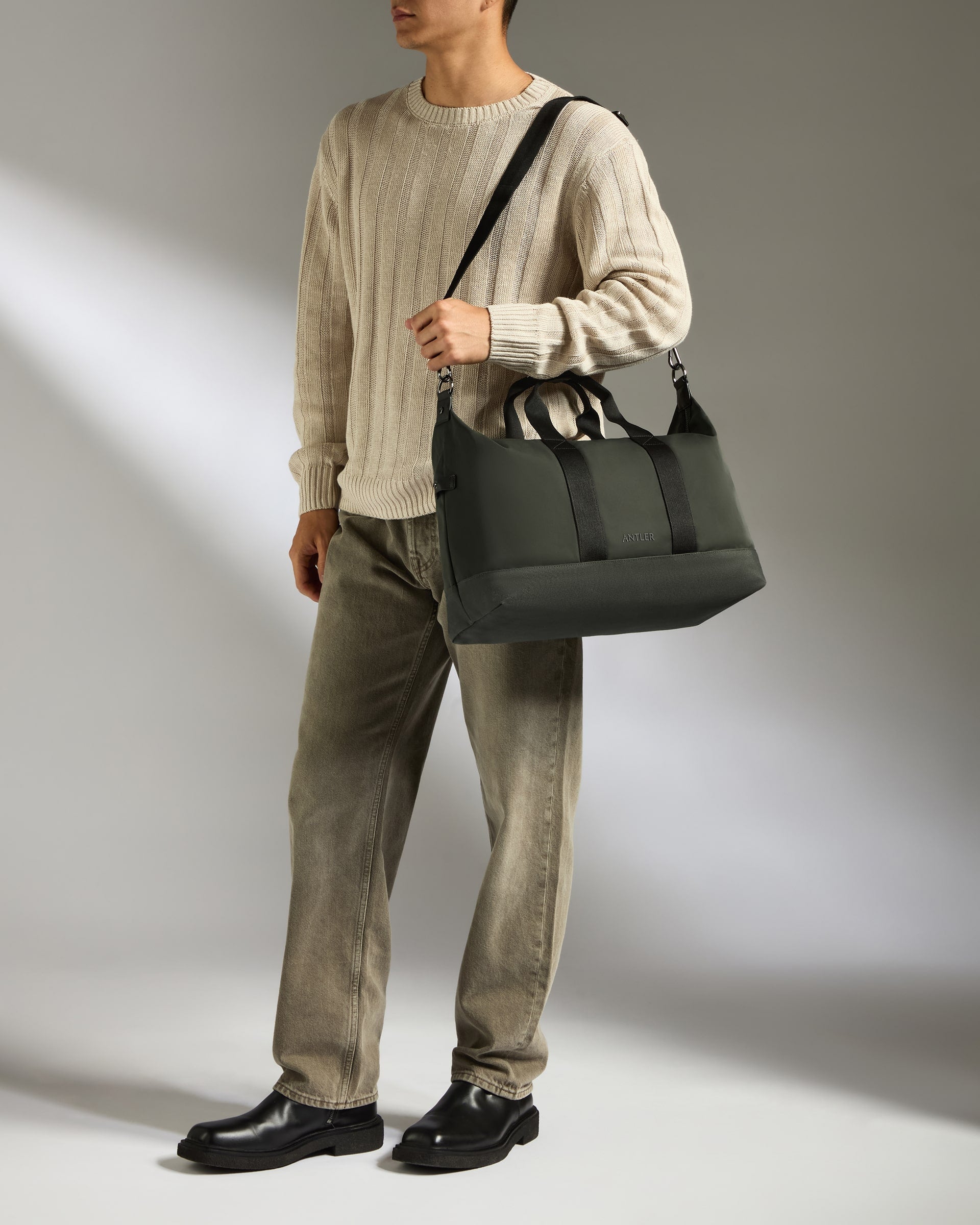 Person holding a black bag against a neutral background