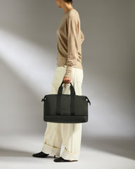 Person holding a black duffel bag against a neutral background