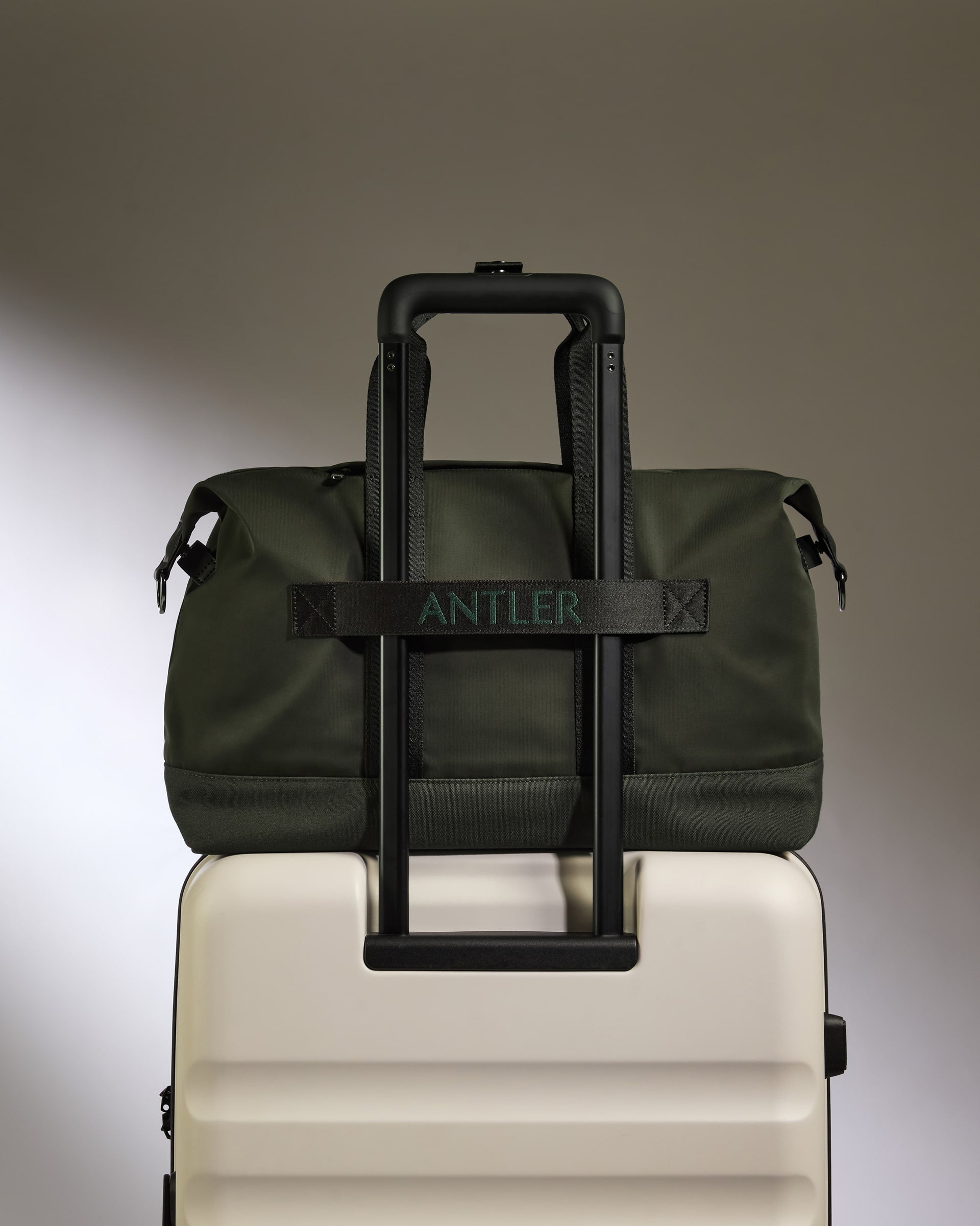 Green duffel bag with black handle on a white suitcase against a gray background