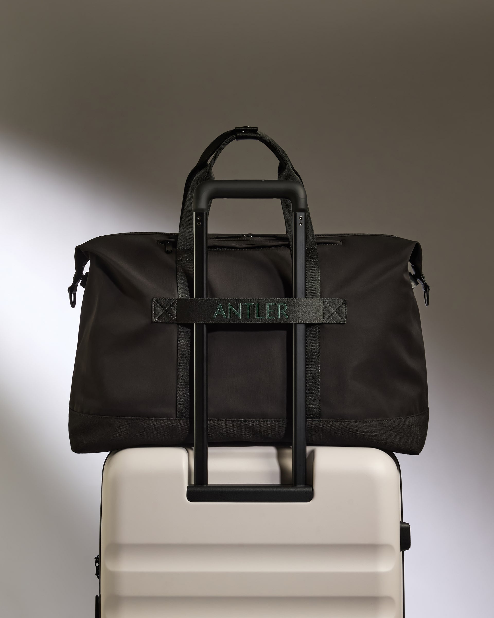 Black duffel bag with 'ANTLER' branding on a beige suitcase against a gradient background
