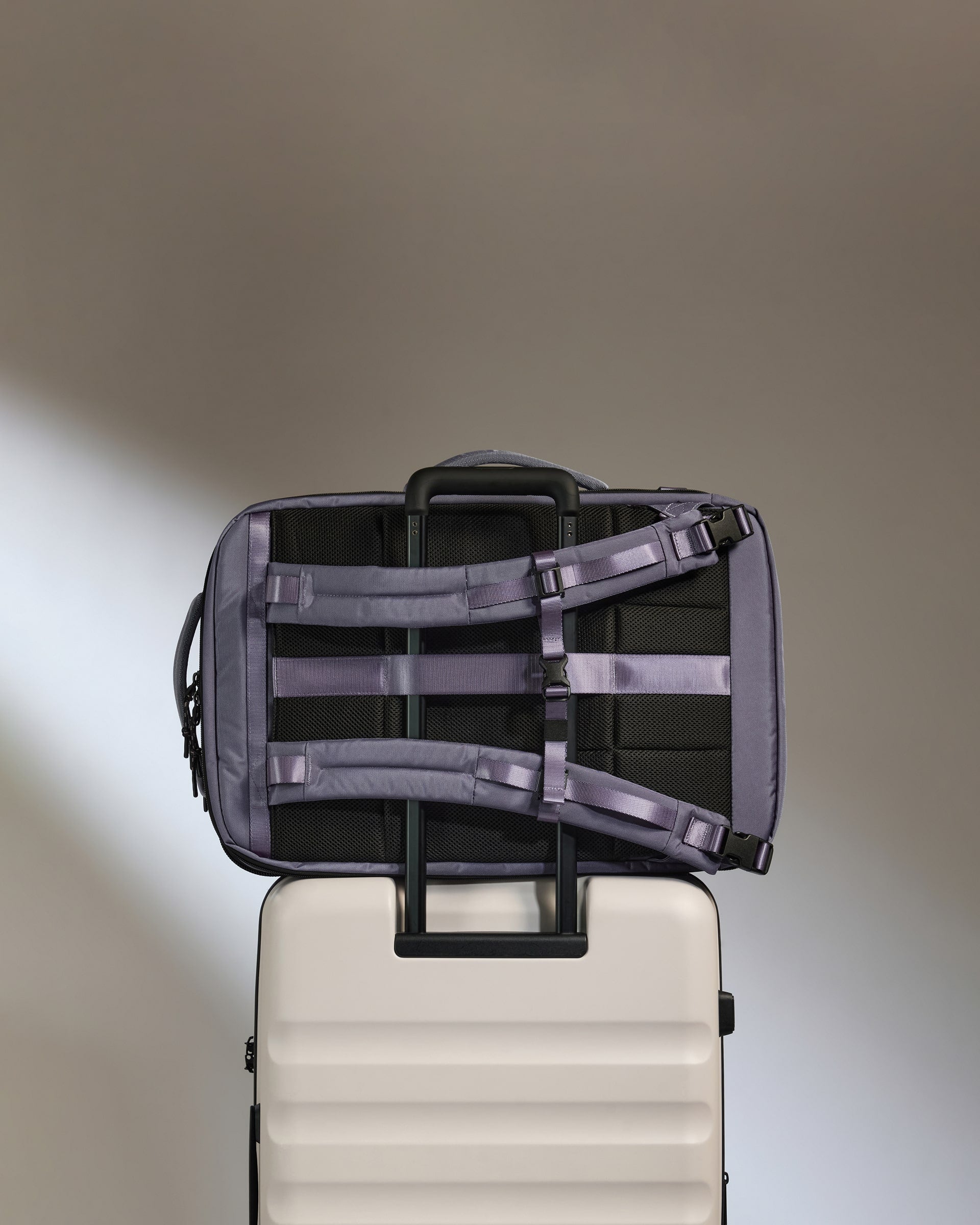 Black backpack with straps on top of a beige suitcase against a neutral background