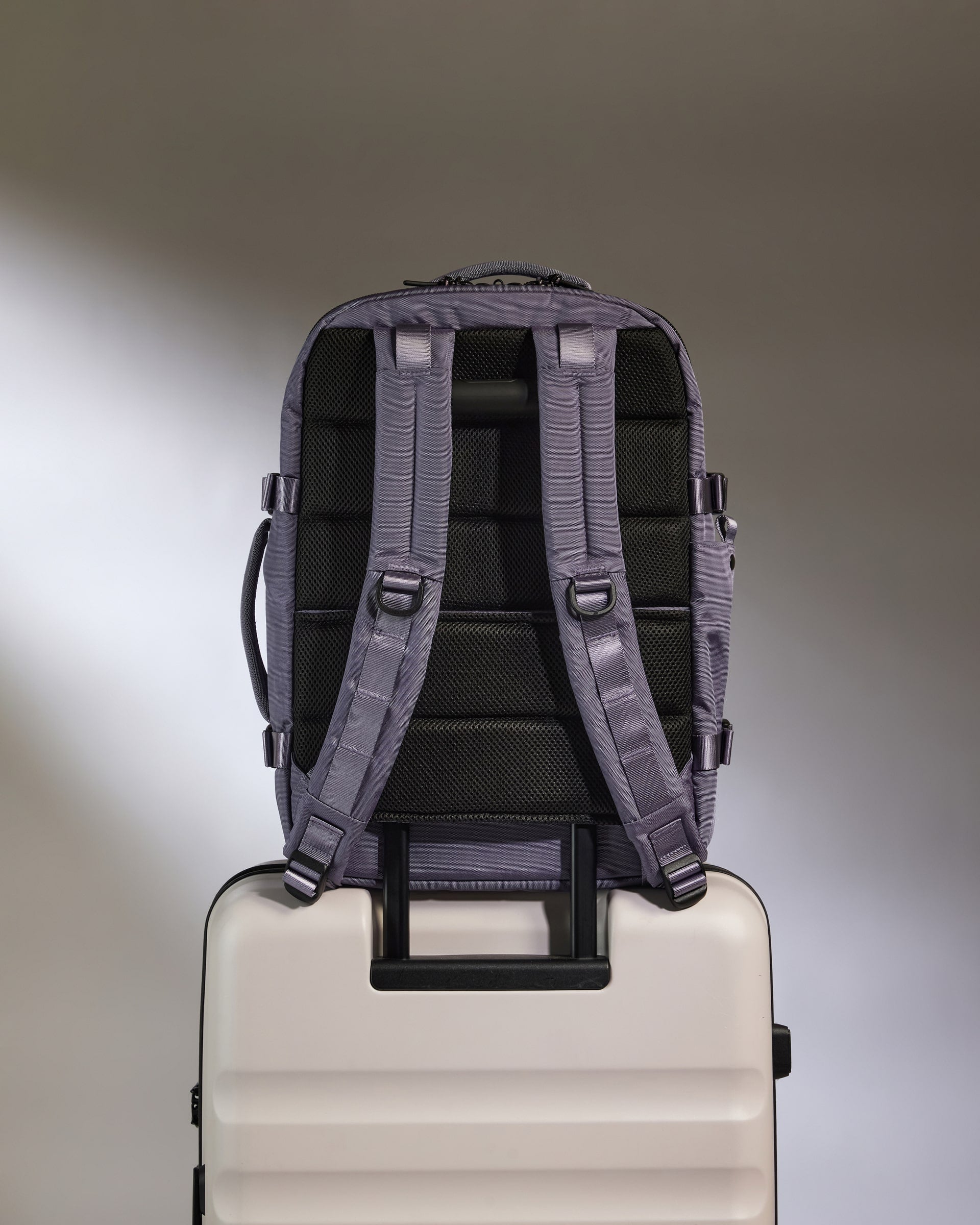 Backpack on top of a suitcase with a neutral background