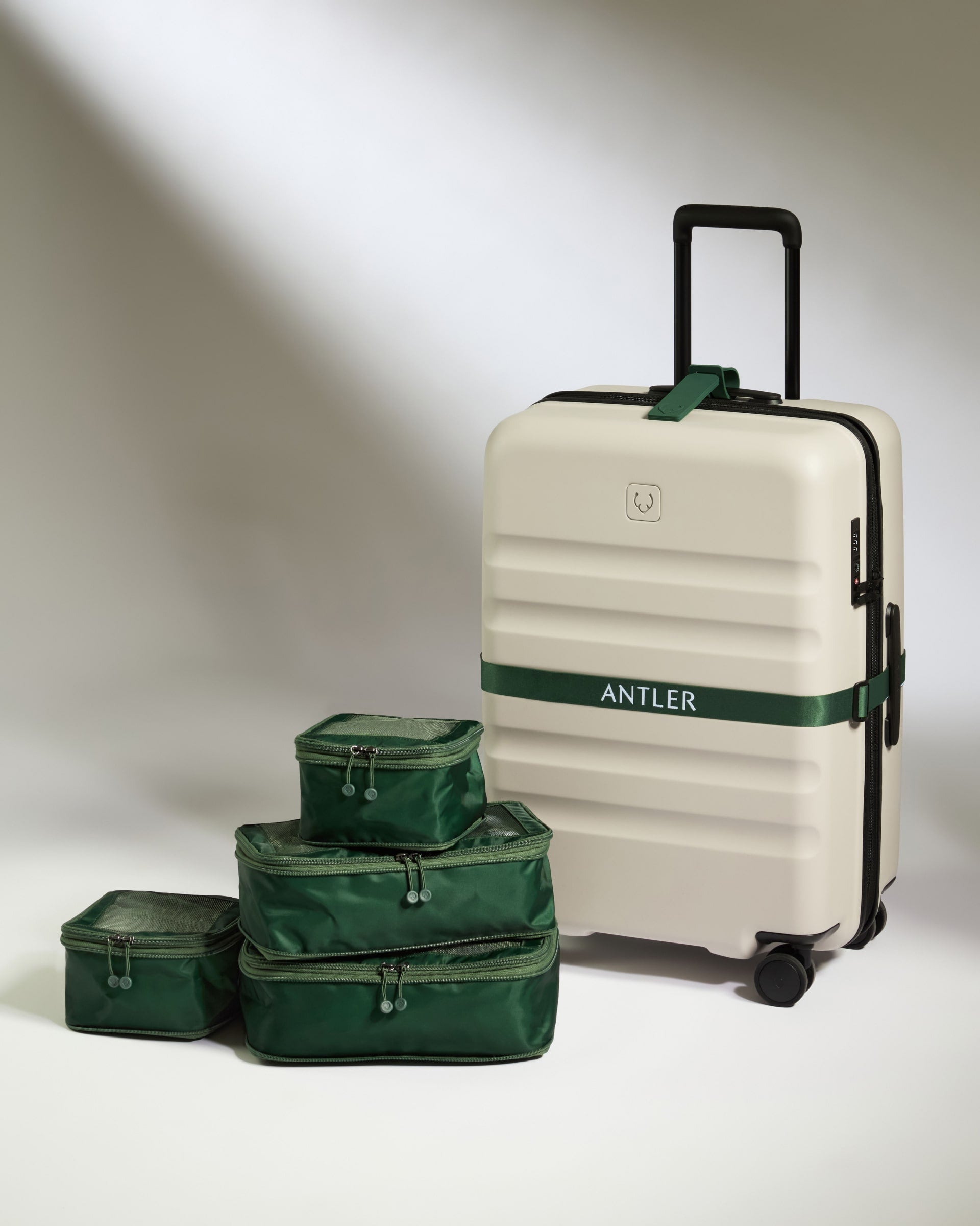Beige suitcase with green straps and matching green packing cubes on a white background