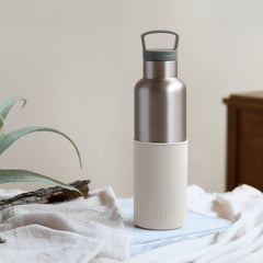Silver and white insulated bottle on a light surface with a plant in the background