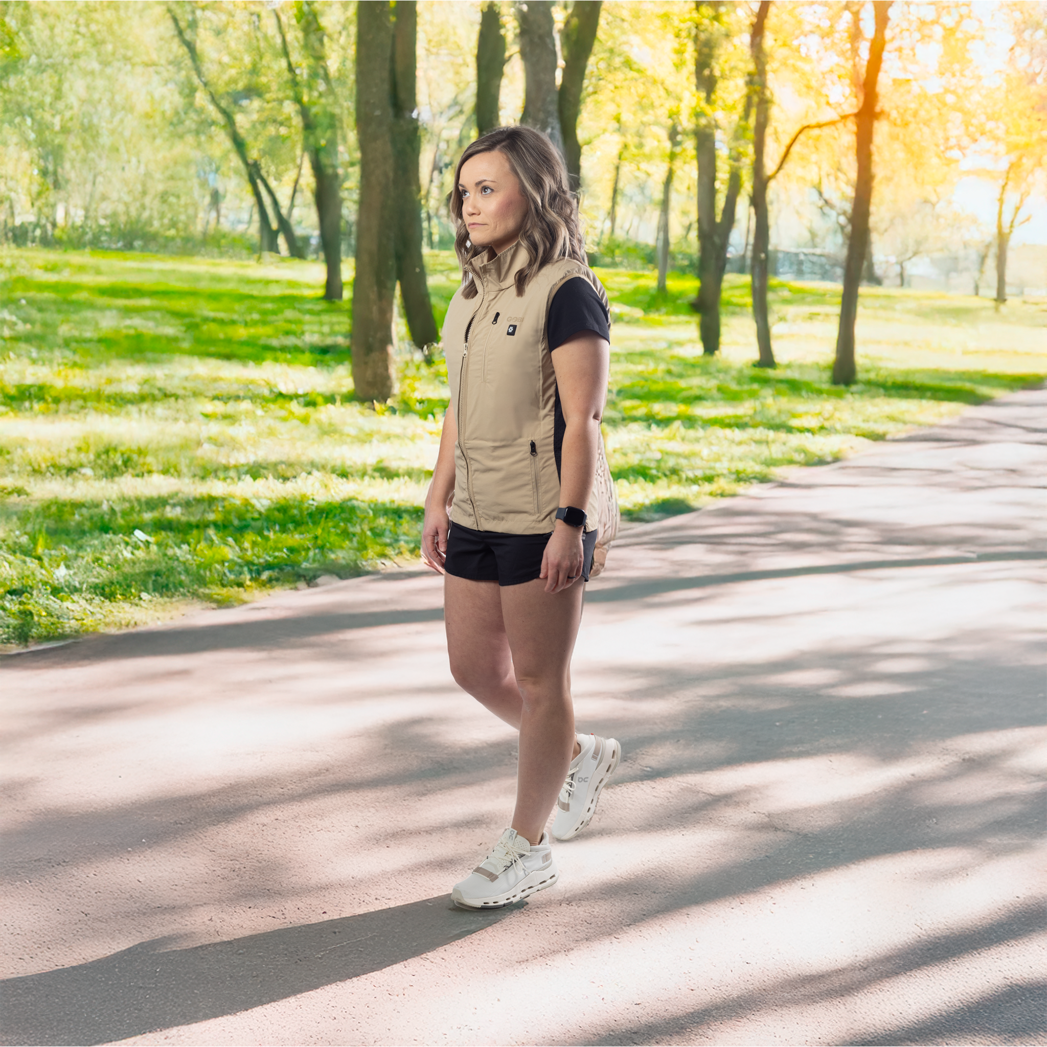 Woman walking in a park wearing a beige vest and black shorts.