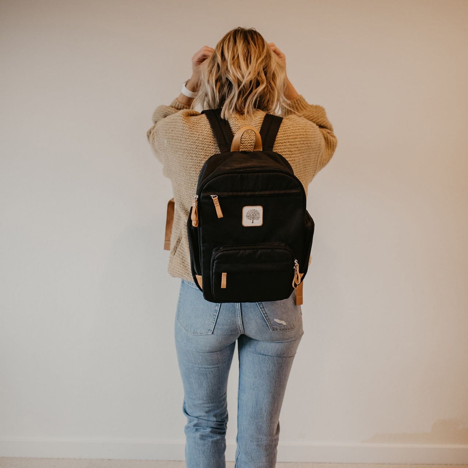 Person wearing a black backpack with a visible brand logo against a plain background