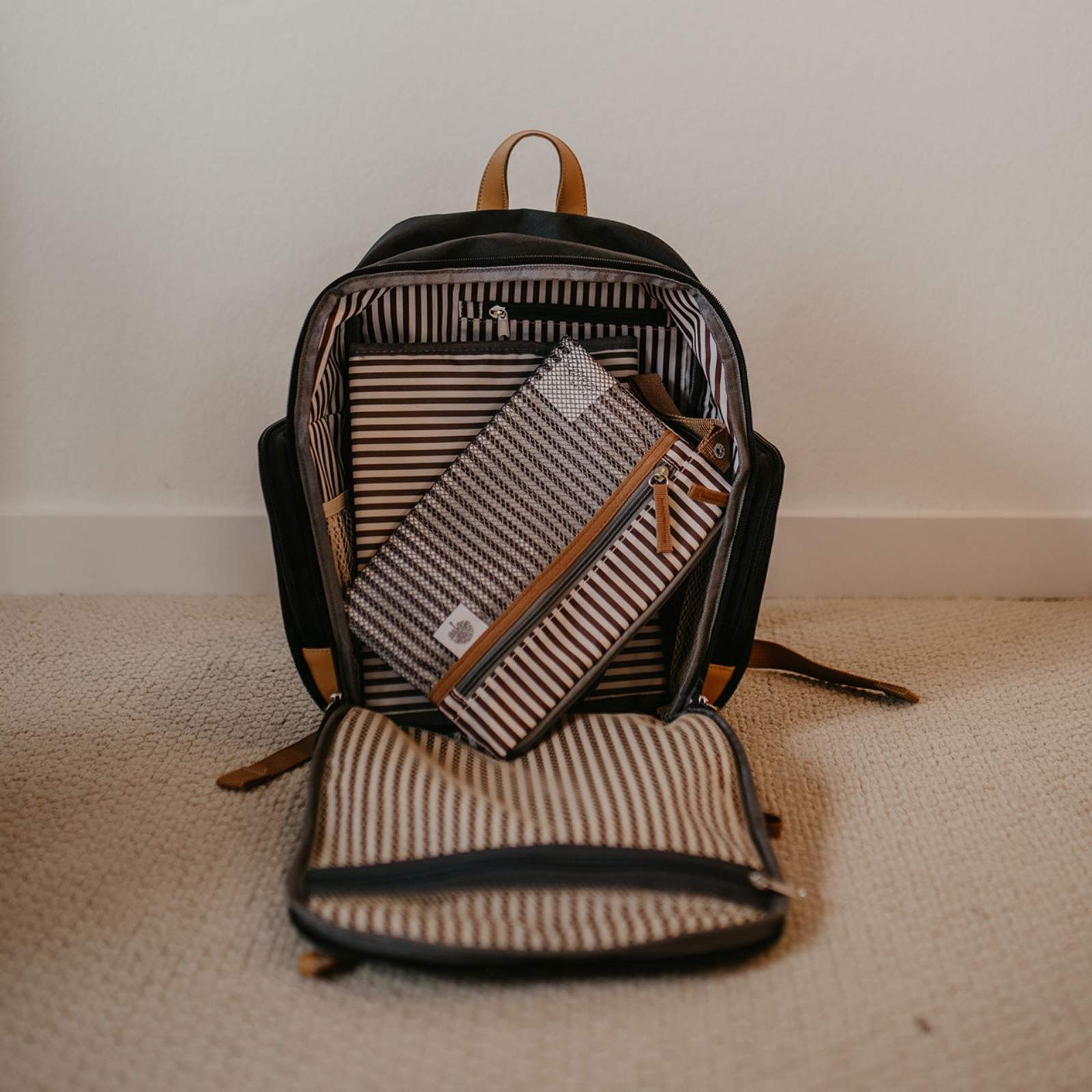 Black backpack with striped pouches on a beige surface