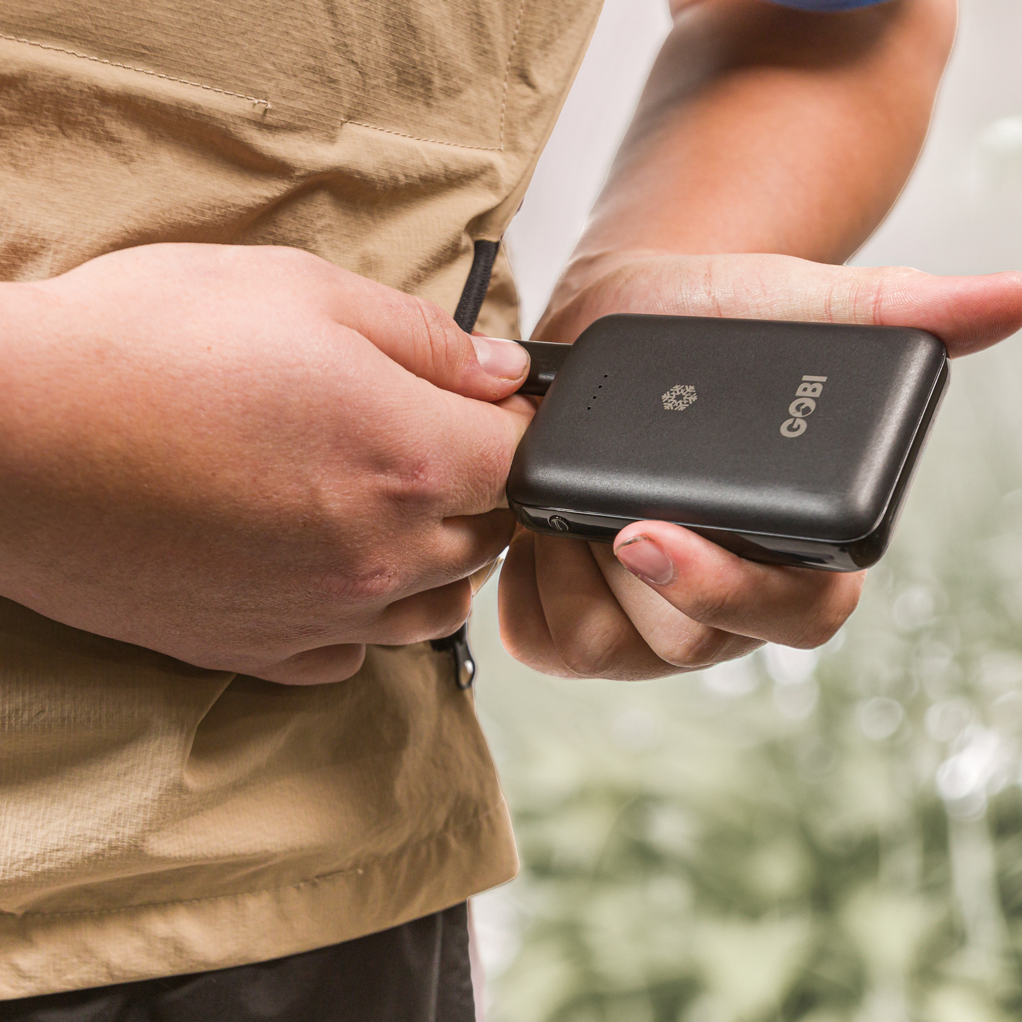Person holding a black portable charger with a blurred natural background