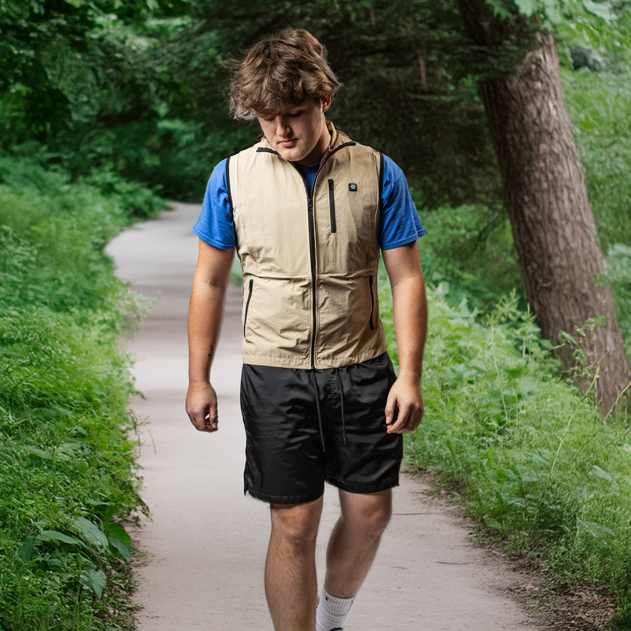 Person walking on a path in a natural setting wearing a beige vest and blue shirt.
