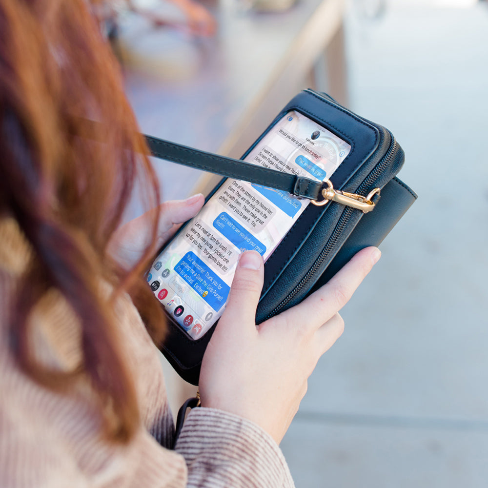 Person holding a phone with text messages displayed, using a black handbag as a stand.