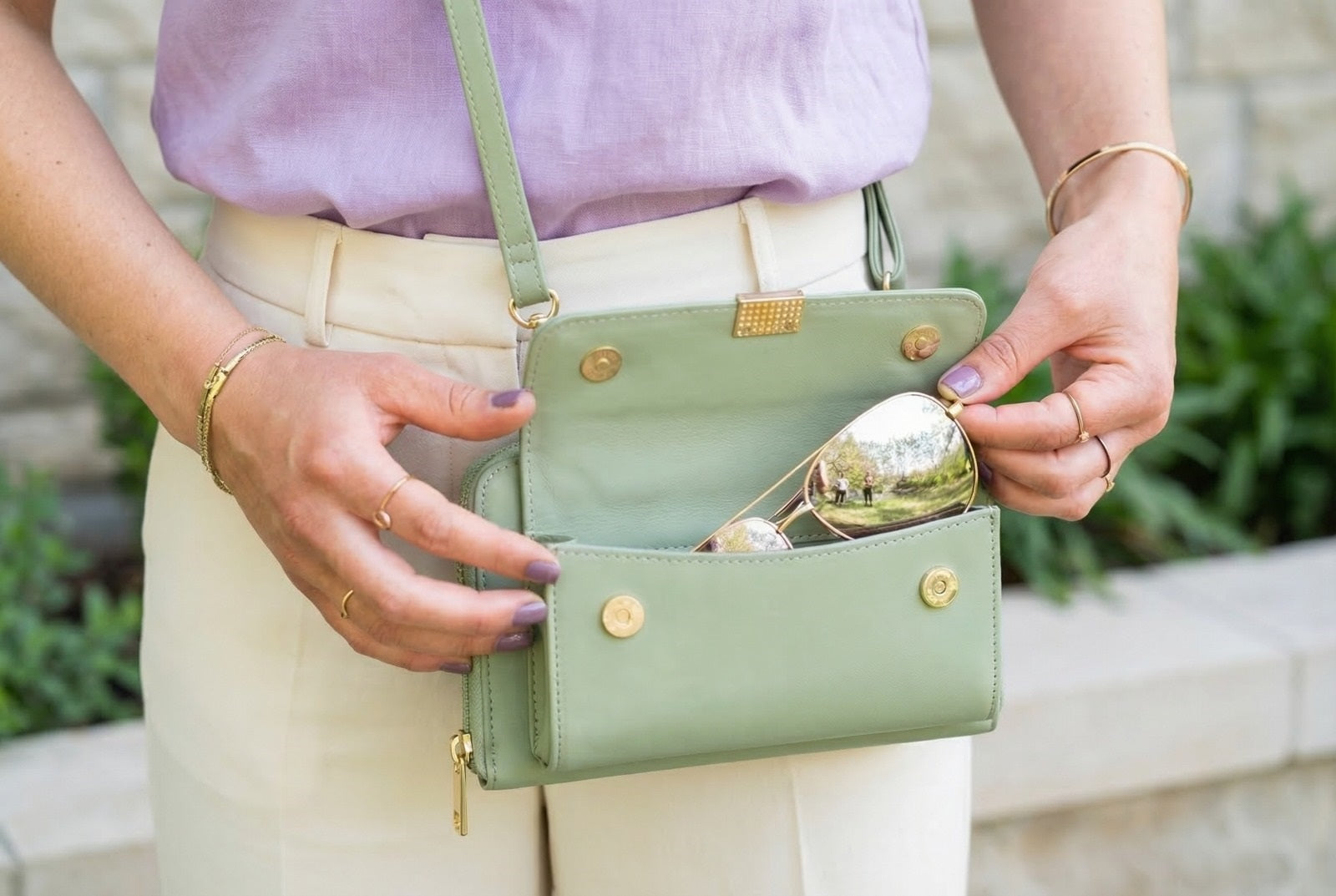 Person holding a green handbag with gold accents outdoors