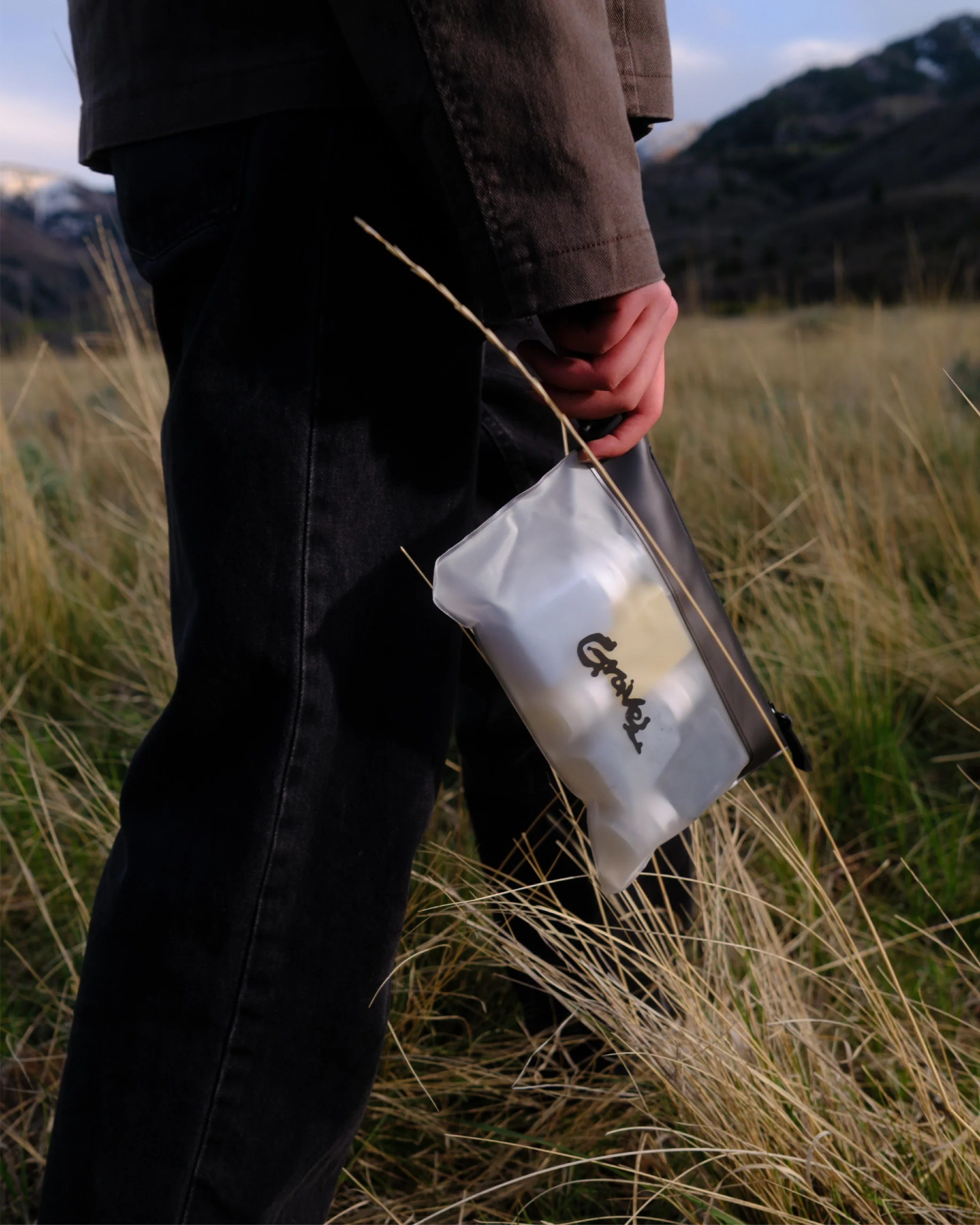 Person holding a clear bag with a logo in a grassy field