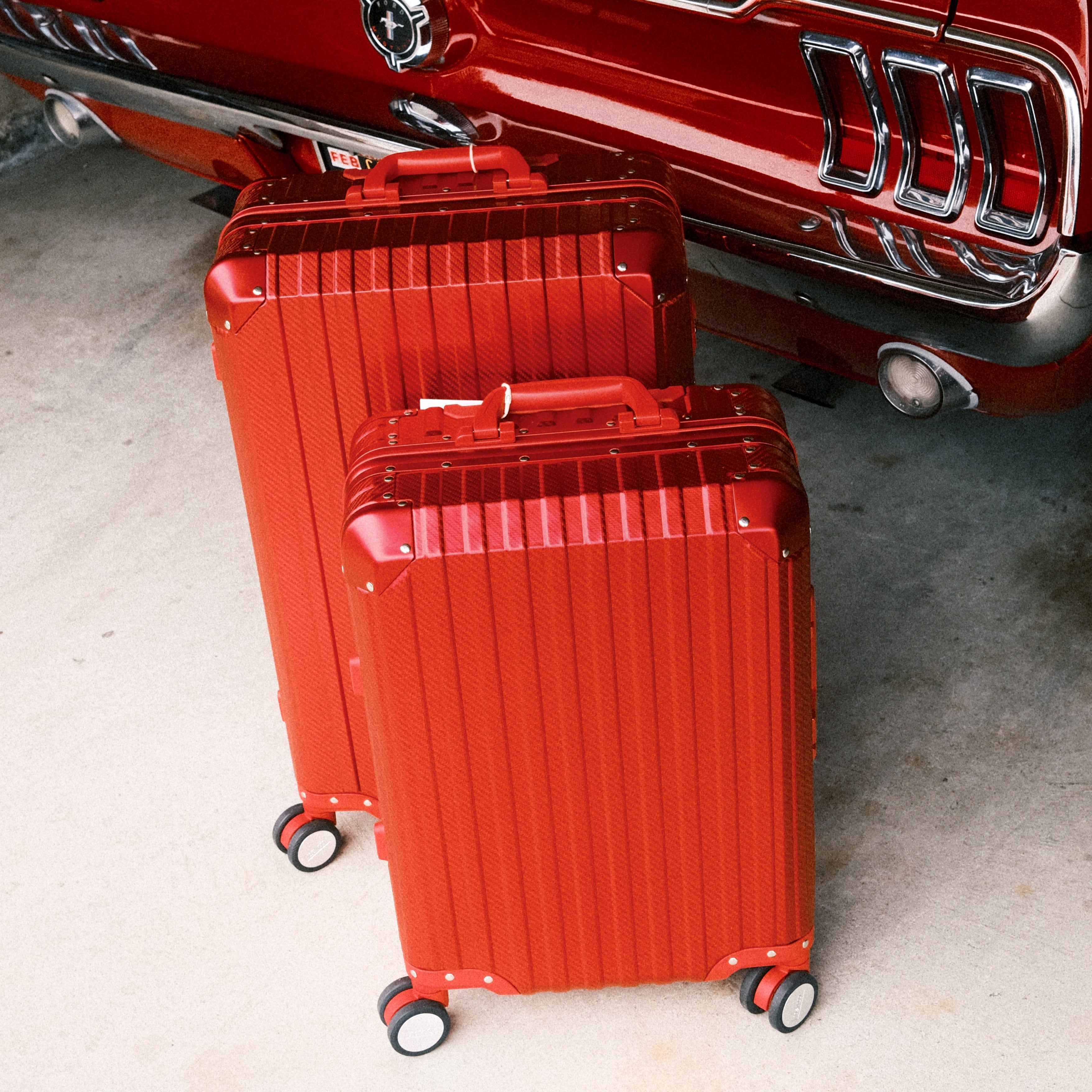 Two red suitcases in front of a classic car