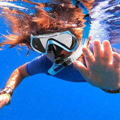 Person snorkeling underwater with a clear blue sky reflection