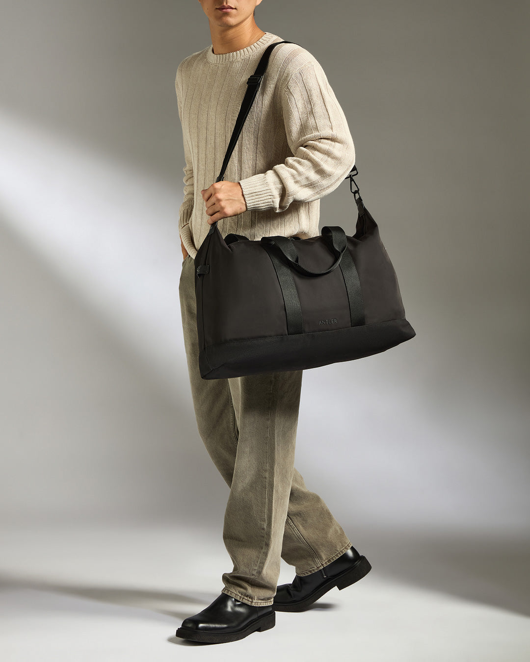 Person holding a black duffel bag against a neutral background