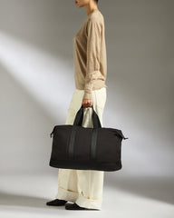 Person holding a black duffel bag against a neutral background