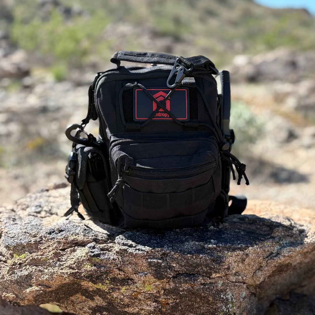 Black tactical backpack with a visible brand logo on a rock in a natural setting