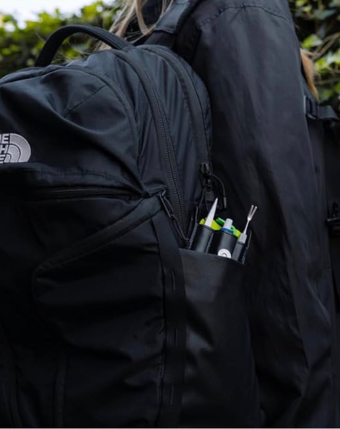 Person wearing a black backpack with a tool pouch containing various items.